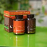 na zelenom stolu se nalaze dve bočice GrandCaps čage sa dihidrovercetinom koje simbolišu dnevnu i noćnu formulu. Iza njh nalazi se kutija u kojoj ruski preparat dolazi.