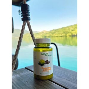 na slici je "rhodiola rosea", adaptogena biljka koja oslobađa telo od psihofizičkog stresa. Slika sadrži bočicu biljnog čaja na drvenoj podlozi, dok su u pozadini plave nijanse jezera i zelene nijanse šume koji simobolišu prirodu i zdravlje, čemu je preparat namenjen